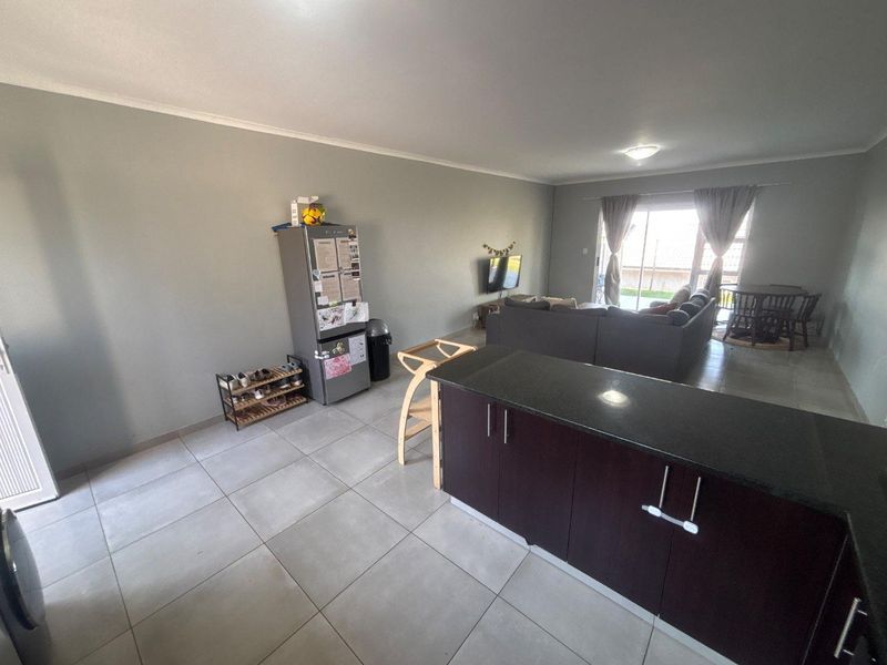 Open-plan living area featuring a kitchen island with dark cabinetry and stone countertops, flowing into a spacious lounge with access to the patio.