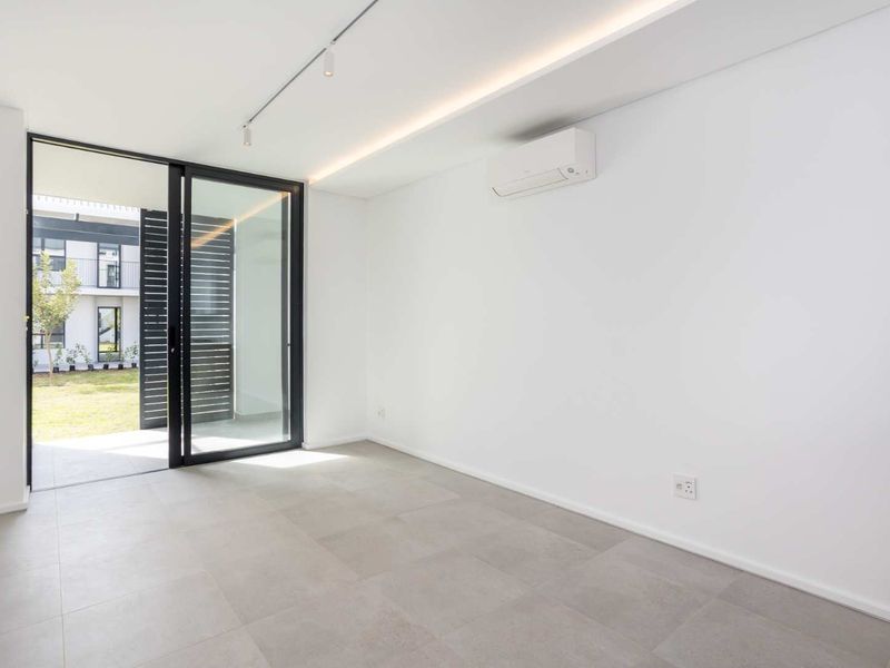 A bright, modern, and empty living room featuring large sliding glass doors leading to a patio, tiled floors, and a wall-mounted air conditioning unit.