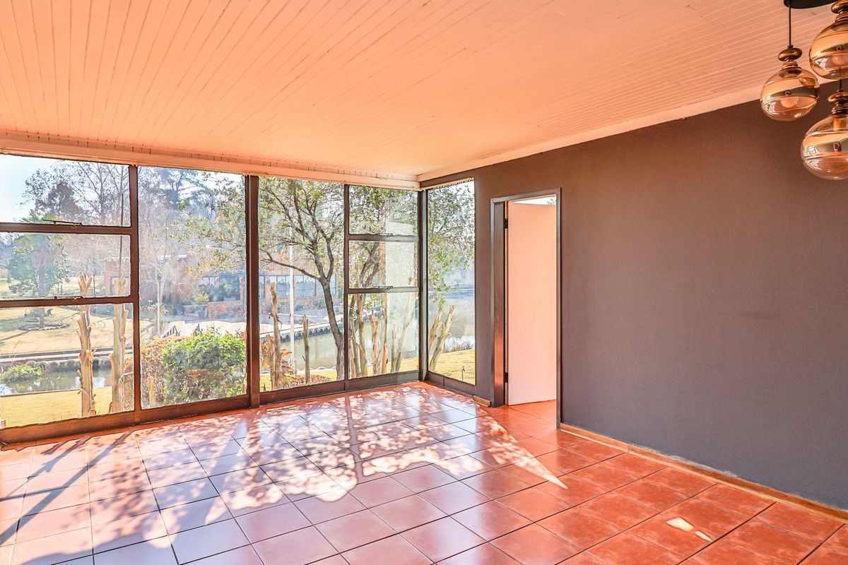 A bright, empty living room featuring large floor-to-ceiling windows with garden views, tiled flooring, and a distinctive beaded timber ceiling.