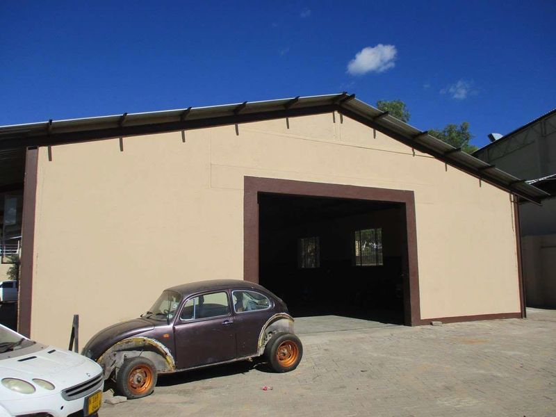 Front view of an industrial warehouse building featuring a large entrance, metal roofing, and paved exterior area.