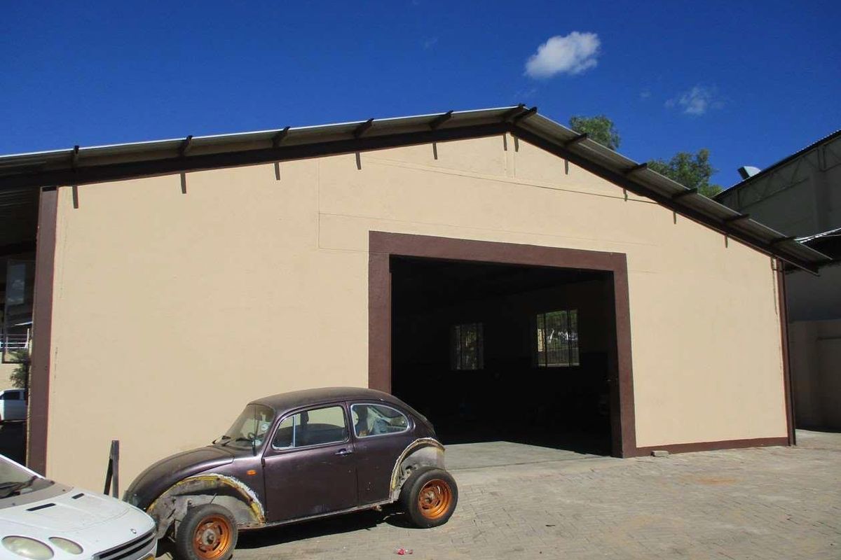 Front view of an industrial warehouse building featuring a large entrance, metal roofing, and paved exterior area.