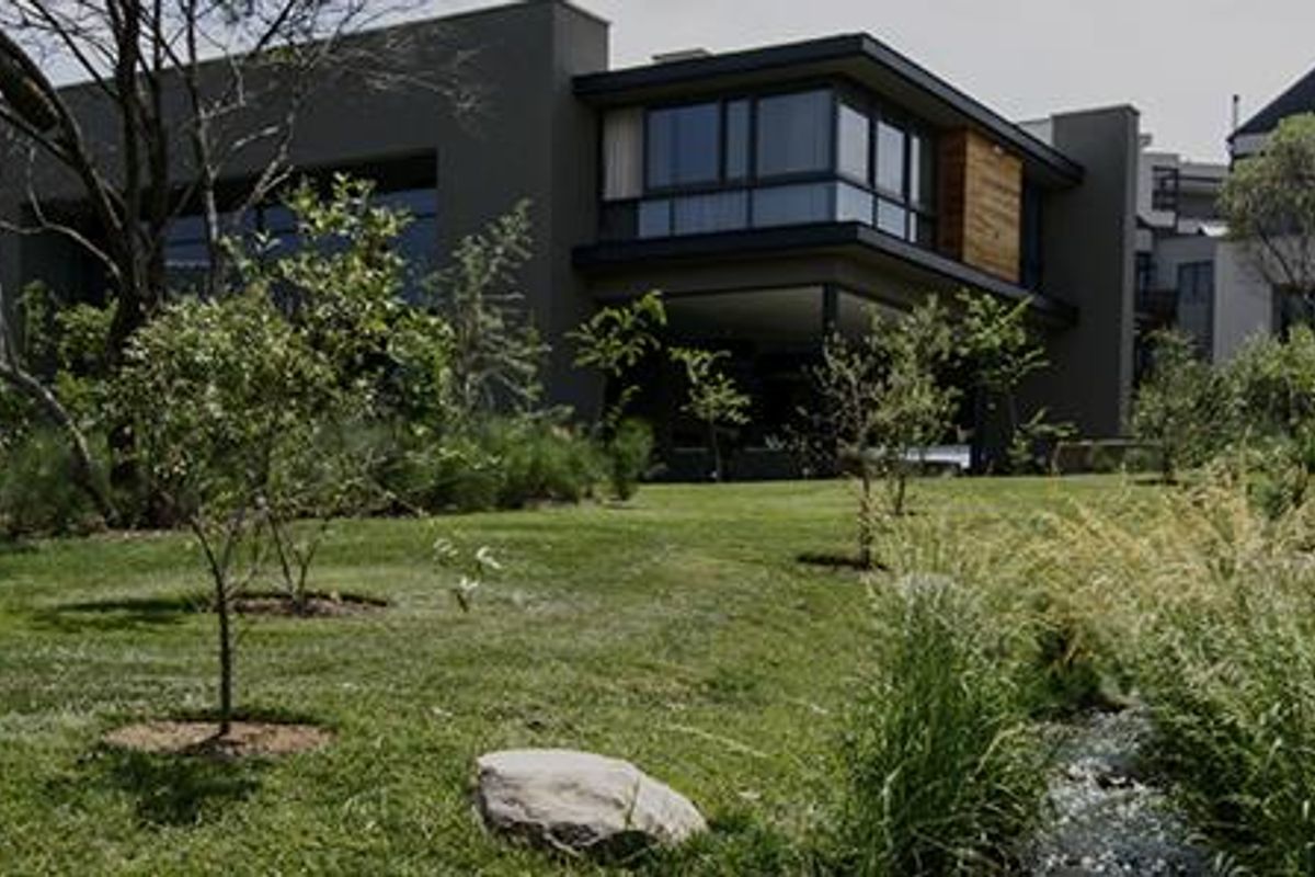 A modern architectural residence set within a lush, landscaped garden featuring mature trees and a natural stream.