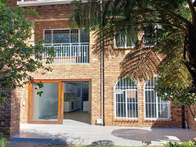 Rear view of a face brick townhouse featuring a paved patio, sliding glass doors, and an upper-level balcony with security bars.