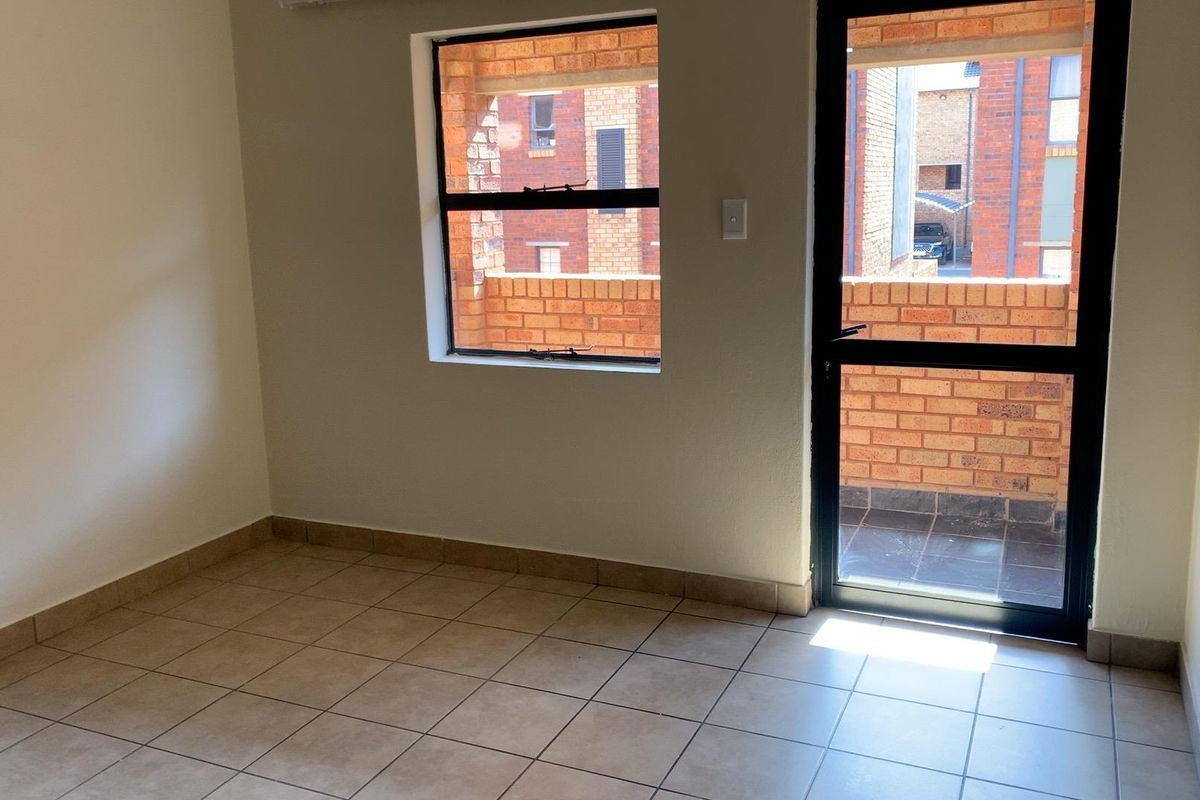 A bright, empty bedroom featuring tiled flooring, a window, and a glass-panelled door providing access to an outdoor balcony area.