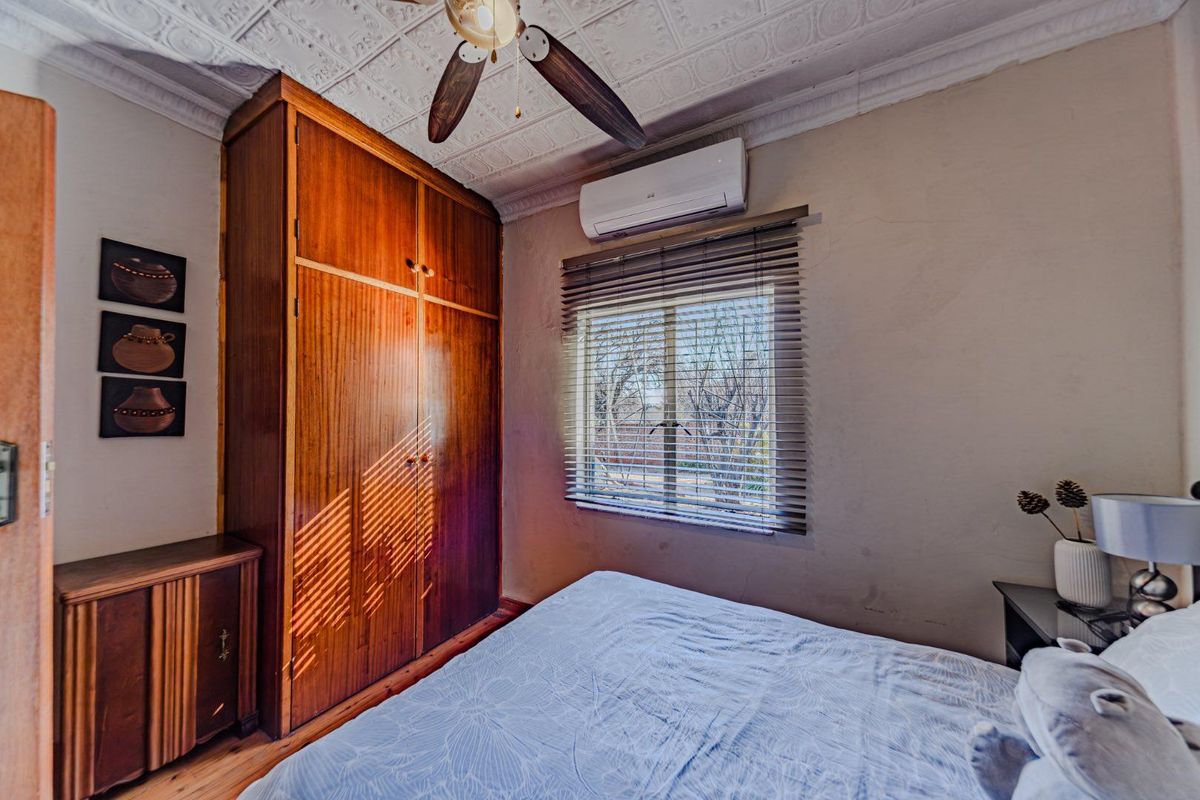 A bedroom featuring a built-in wooden wardrobe, split-system air conditioning, a decorative pressed metal ceiling, and timber flooring.