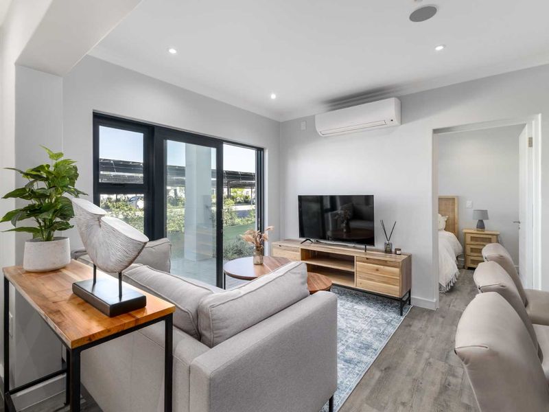 Modern open-plan living area featuring laminate flooring, recessed lighting, a split-system air conditioner, and large sliding glass doors leading to the exterior.