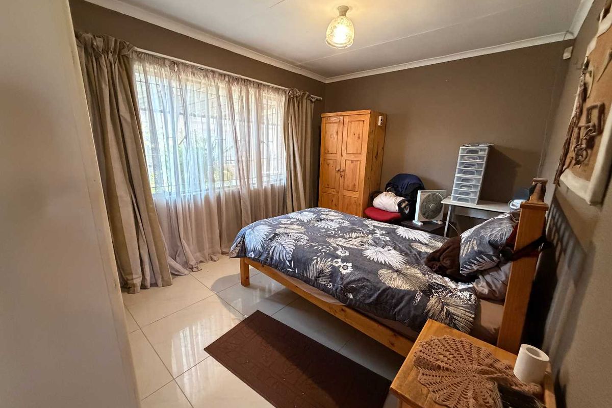 A standard bedroom featuring tiled flooring and large windows with curtain rails, providing a functional space with neutral wall tones.