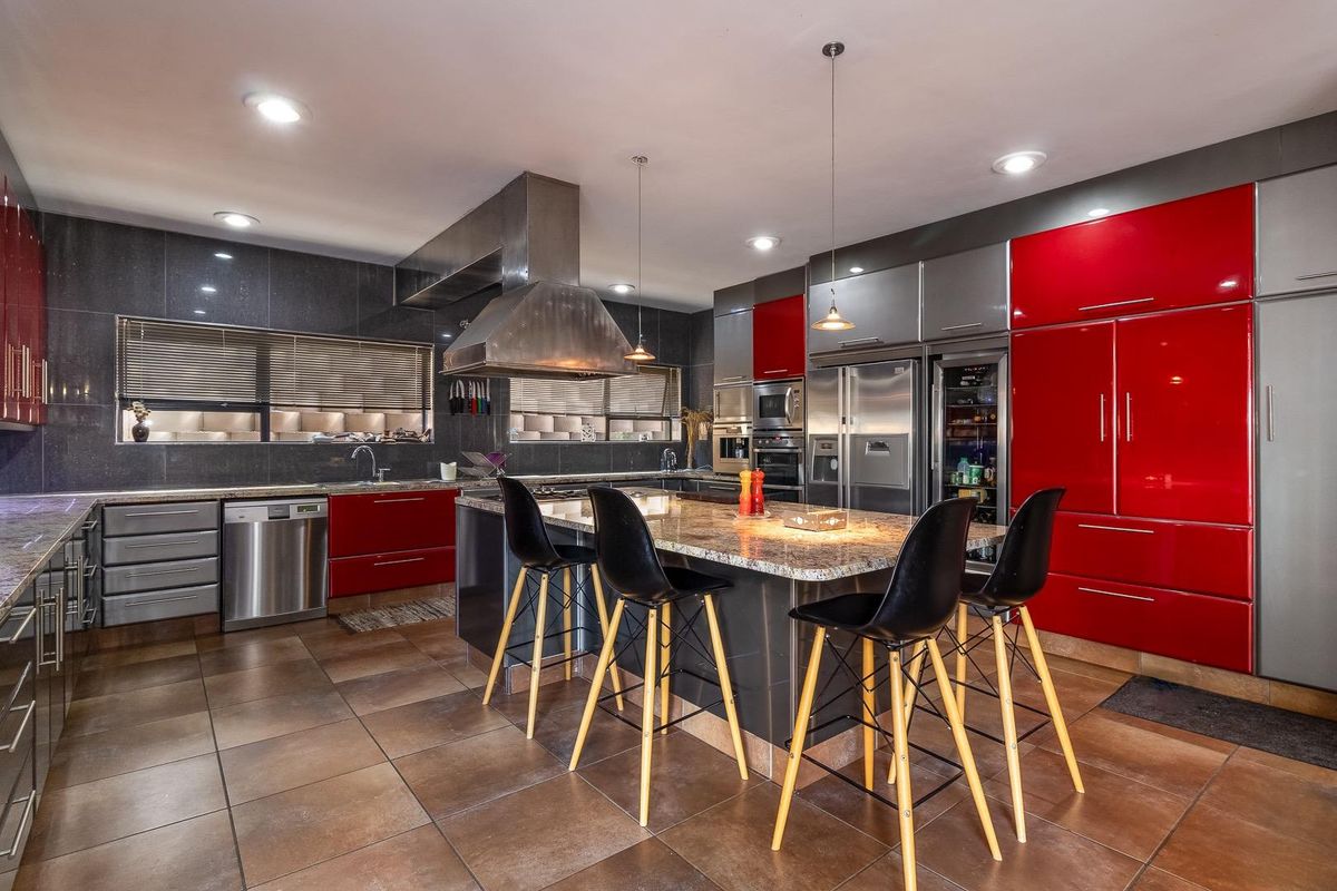 Modern kitchen featuring high-gloss red and grey cabinetry, granite countertops, a central island, and professional-grade stainless steel appliances.