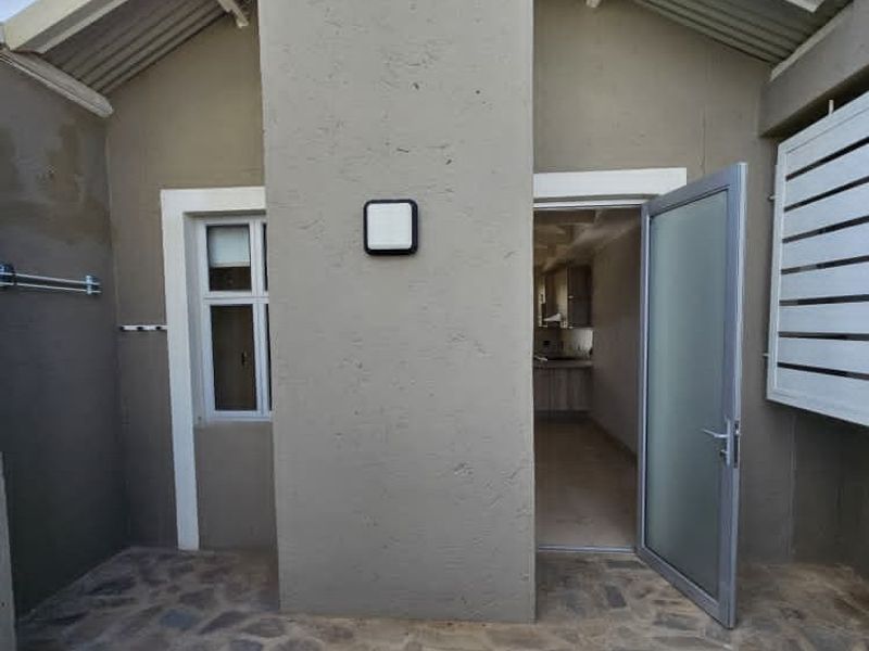 A rear exterior view of the property featuring stone paving, a frosted glass door, and a metal louvre shutter.
