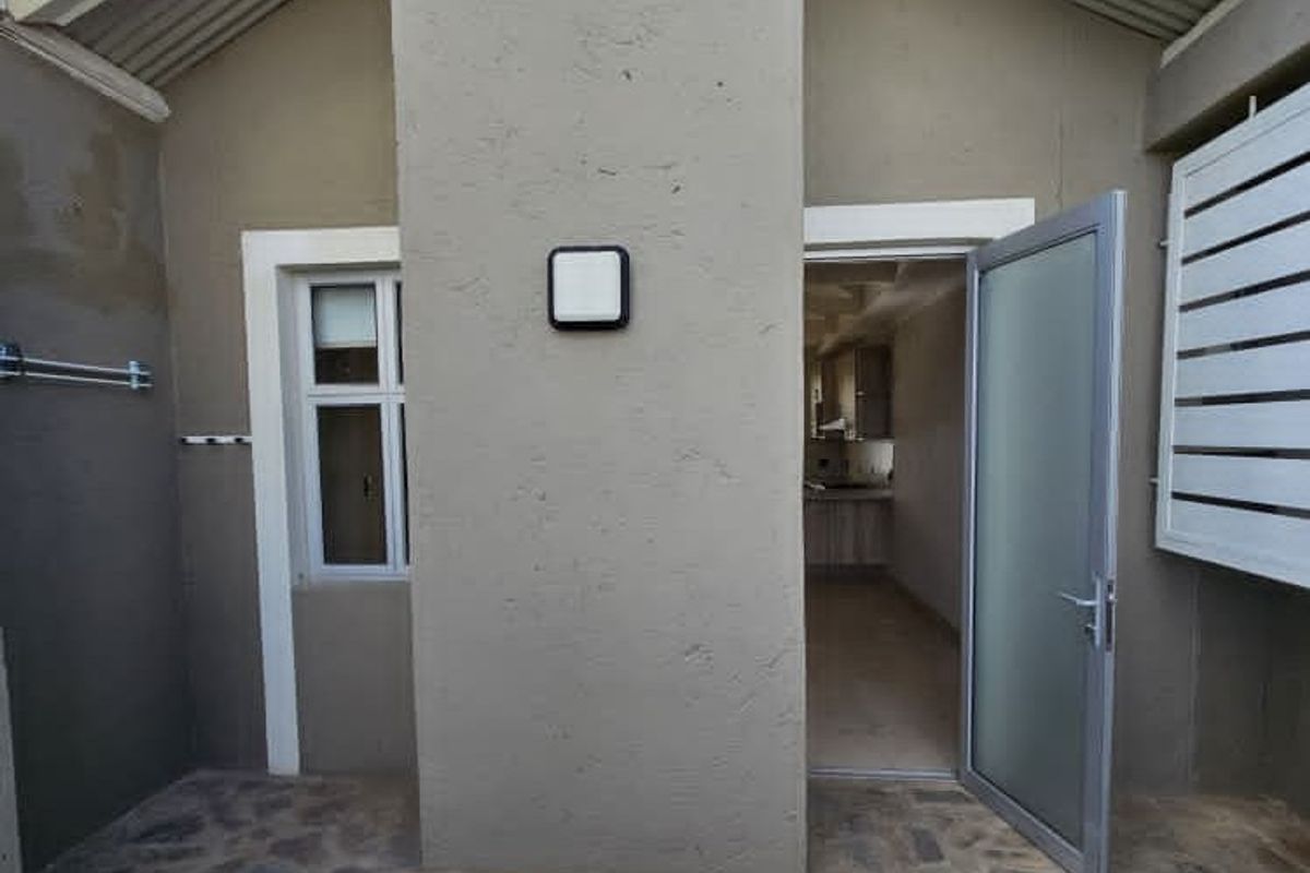 A rear exterior view of the property featuring stone paving, a frosted glass door, and a metal louvre shutter.