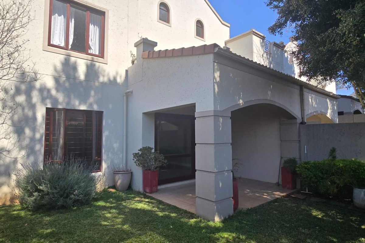 Rear view of the apartment featuring a covered tiled patio with arched columns, sliding glass doors, and access to a private garden area.