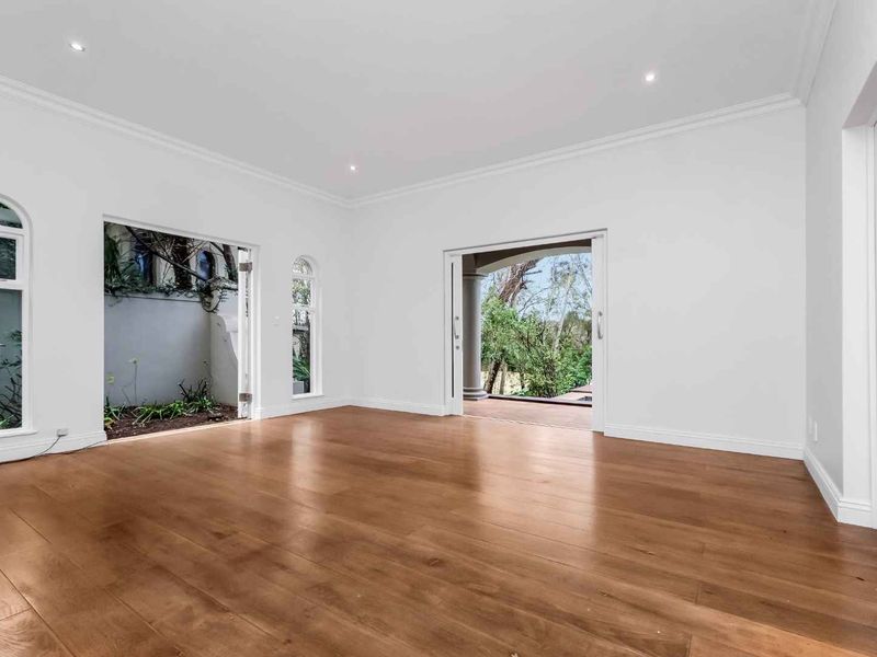 A bright, spacious living area featuring polished timber flooring, recessed downlights, and multiple access points to the outdoor patio and garden.