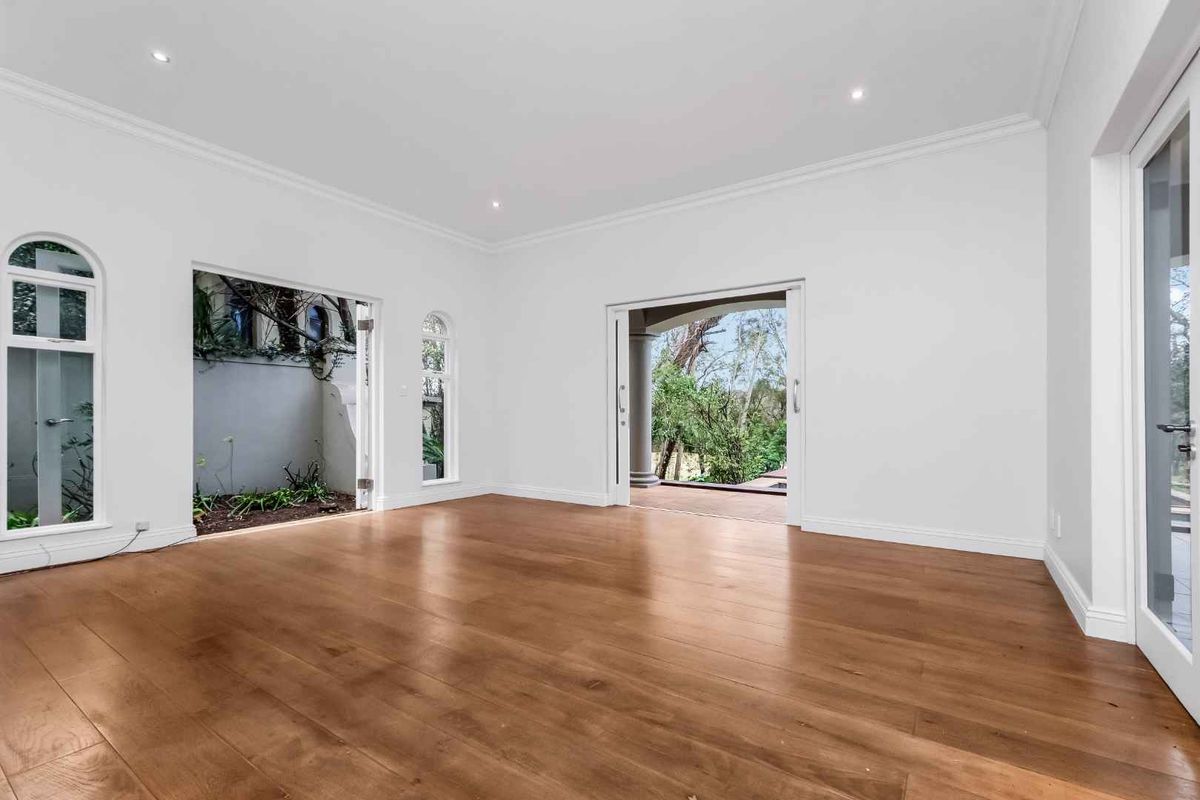 A bright, spacious living area featuring polished timber flooring, recessed downlights, and multiple access points to the outdoor patio and garden.