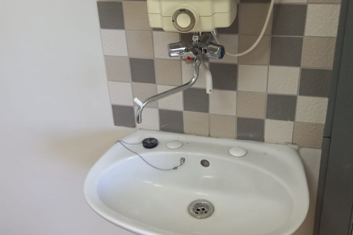 A small office bathroom featuring a wall-mounted basin, tiled splashback, and a wall-mounted water heater unit.