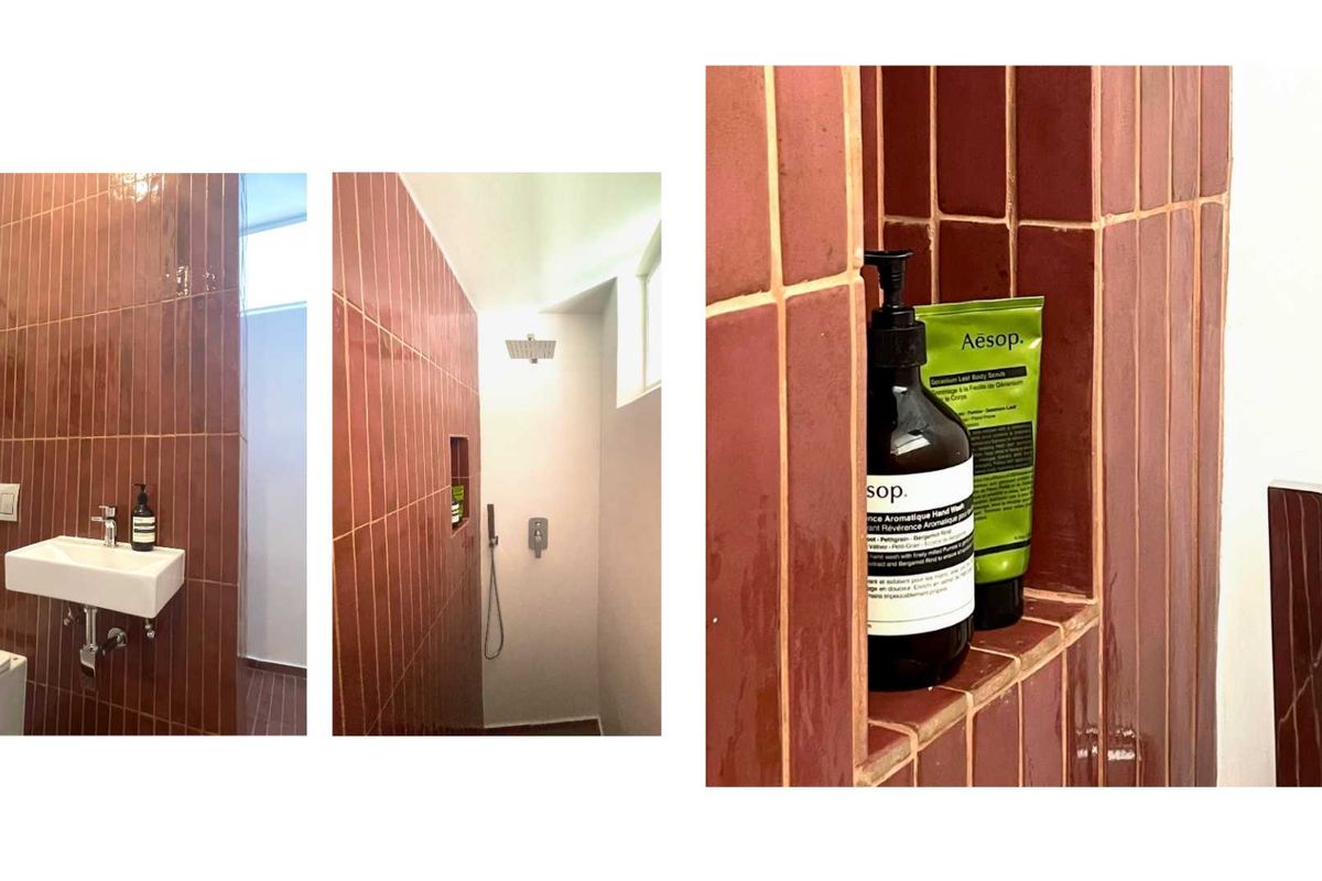 A modern bathroom featuring terracotta-toned vertical ceramic wall tiles, a wall-mounted basin, and a walk-in shower with a recessed storage niche.