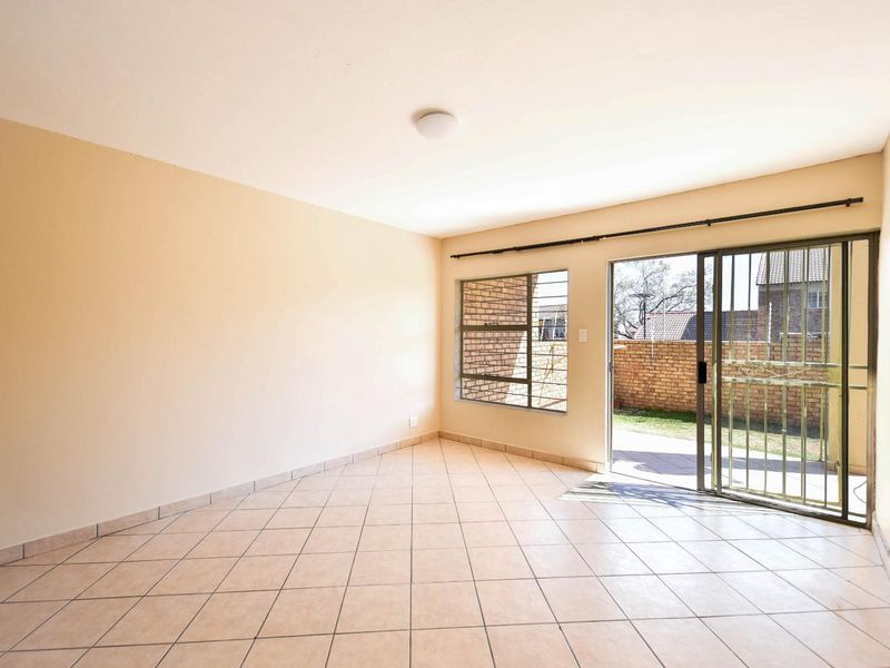An empty living room featuring tiled flooring, a sliding glass door with security gate, and access to an outdoor patio area.