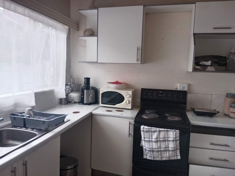 A functional kitchen featuring white cabinetry, laminate countertops, a stainless steel sink, and a freestanding electric stove with tiled splashback.