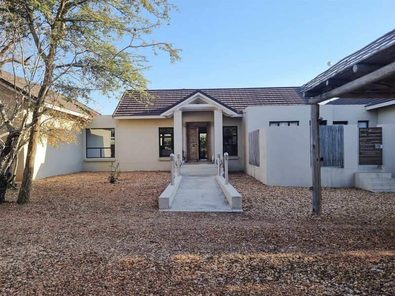 Front elevation of a single-story house featuring a central entrance with a concrete walkway, tiled roof, and a timber pergola structure.