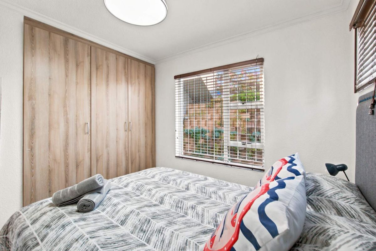 A well-maintained bedroom featuring built-in wooden cupboards, venetian blinds, and a modern flush mount ceiling light.