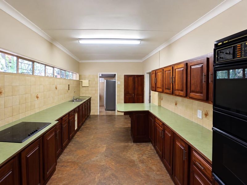 Spacious kitchen featuring extensive wooden cabinetry, laminate countertops, built-in double oven, electric hob, and tiled backsplash with a functional layout.