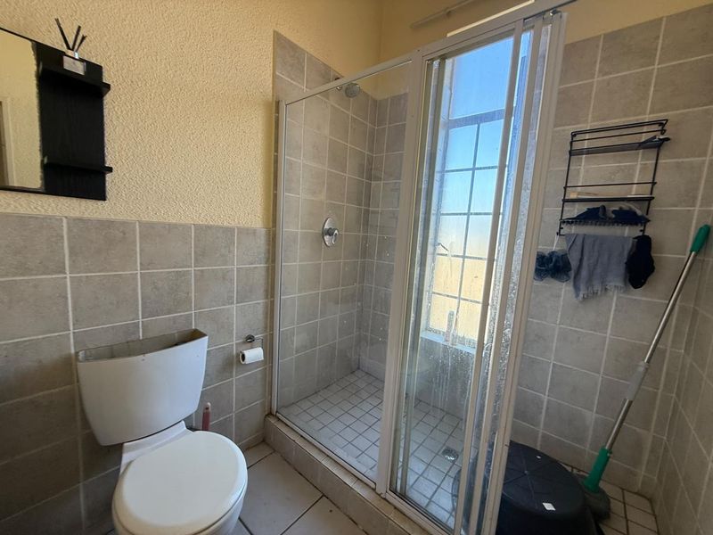 A functional bathroom featuring a tiled shower enclosure and standard toilet, with neutral wall finishes and tiled flooring throughout.