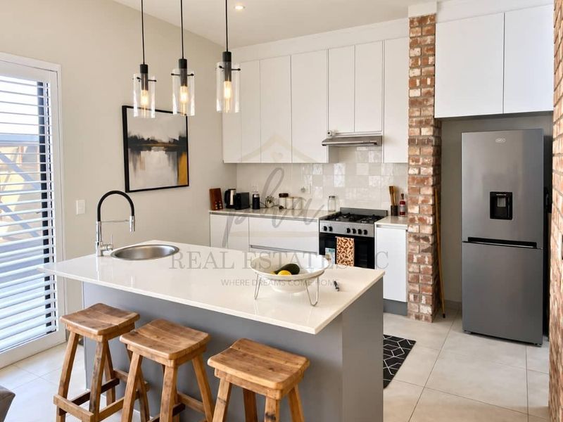 Modern kitchen featuring a central island with quartz countertops, exposed brick accents, built-in appliances, and stylish pendant lighting in an open-plan layout.