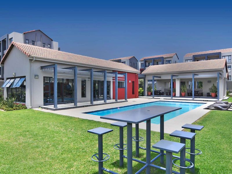 A well-maintained communal pool area featuring a paved deck, pergola structures, and landscaped lawn within a modern apartment complex.