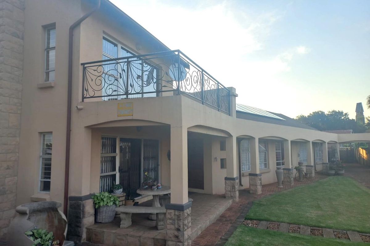 Rear view of the property featuring a covered patio area, a spacious upper balcony with wrought iron railings, and a well-maintained garden.