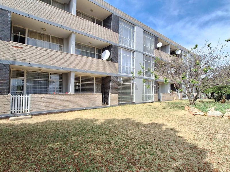 Rear view of a multi-story apartment building featuring brick facade, private balconies with security bars, and a shared garden area.