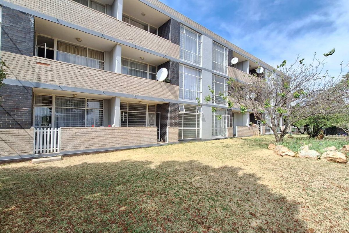 Rear view of a multi-story apartment building featuring brick facade, private balconies with security bars, and a shared garden area.