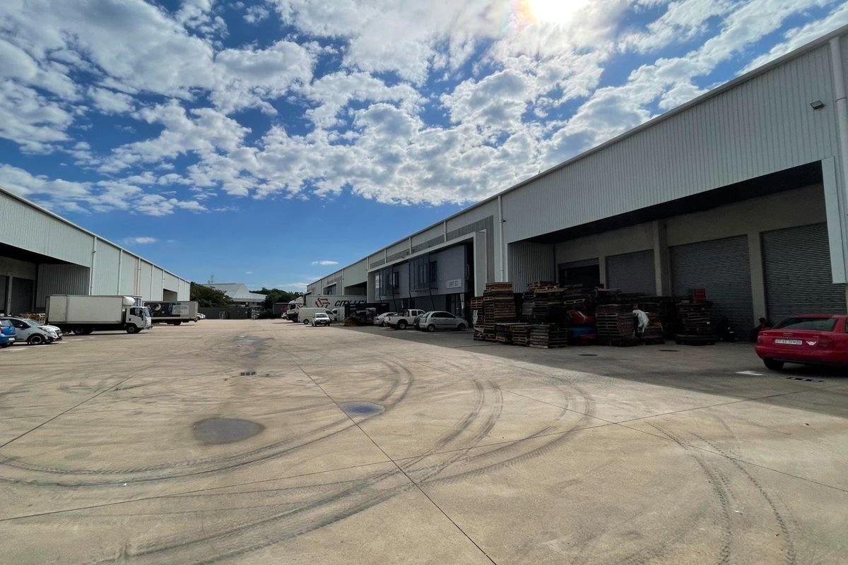 Spacious industrial concrete yard area featuring multiple roller shutter doors and metal-clad warehouse facades, suitable for logistics and heavy vehicle access.