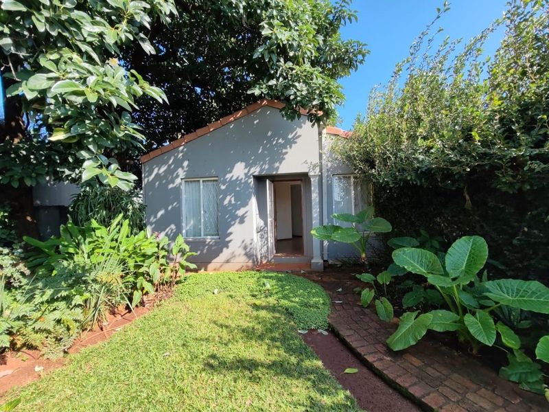A view of the rear exterior of the house featuring a small garden, brick pathway, and mature trees.