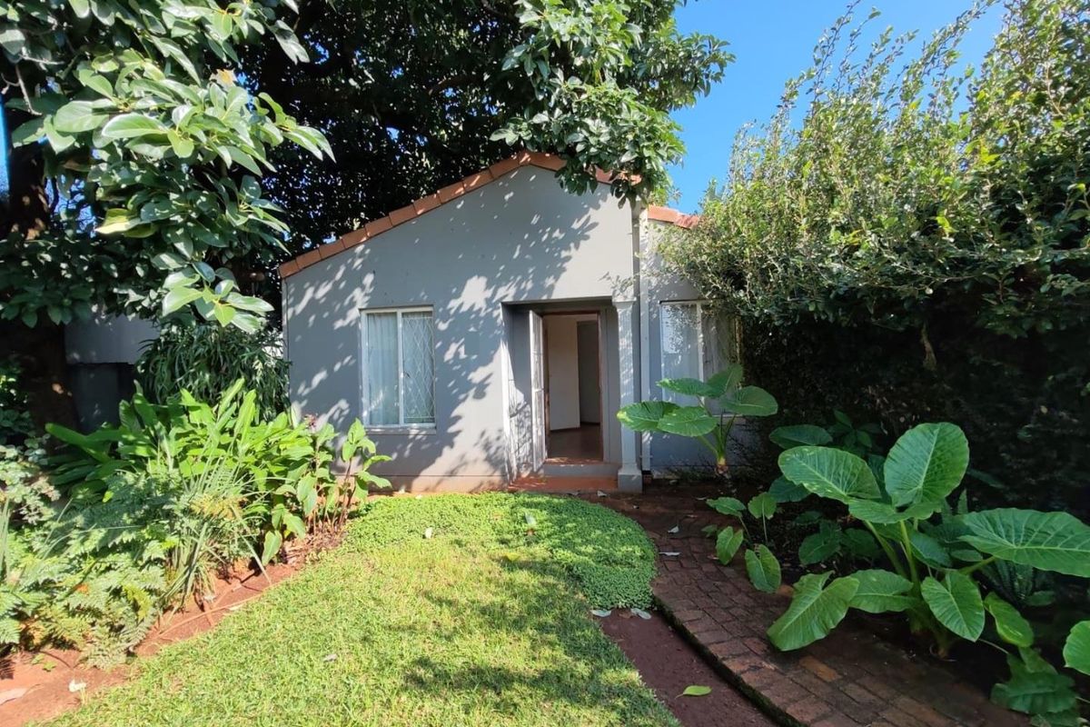 A view of the rear exterior of the house featuring a small garden, brick pathway, and mature trees.