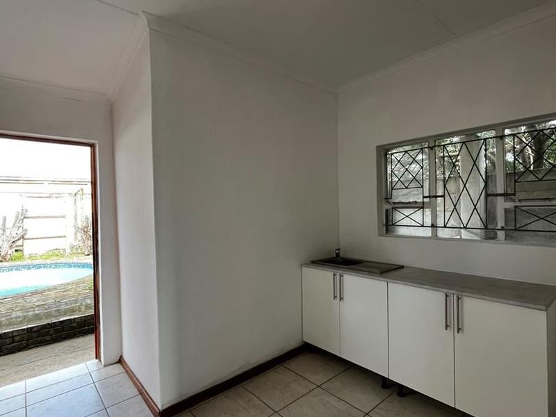 A functional scullery or utility area featuring built-in cabinetry, a sink, tiled flooring, and direct access to the outdoor pool area.