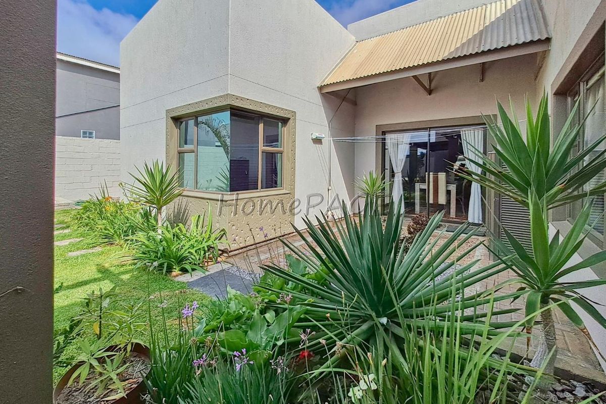 Rear view of the property featuring a landscaped garden, paved patio area, and sliding glass doors providing access to the interior living space.