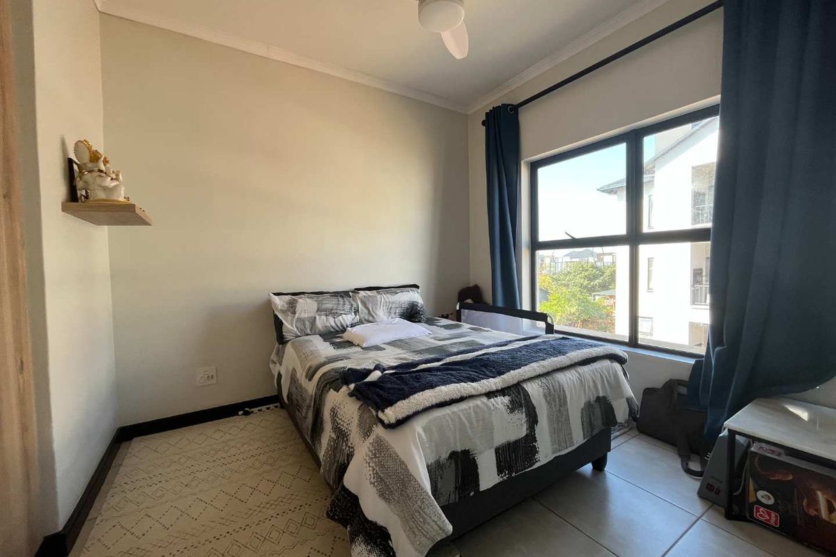 A well-lit bedroom featuring tiled flooring, a ceiling fan, and a large window providing natural light and exterior views.