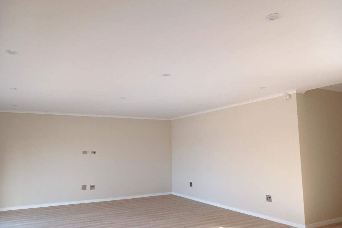 A bright, spacious, and empty living area featuring neutral walls, modern laminate flooring, and recessed ceiling downlights.