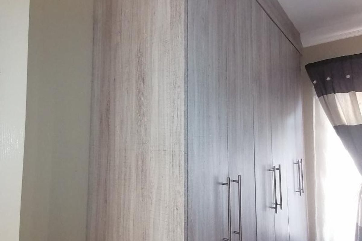 A bedroom featuring modern, light wood-grain built-in cupboards with sleek metal handles, providing ample storage space.