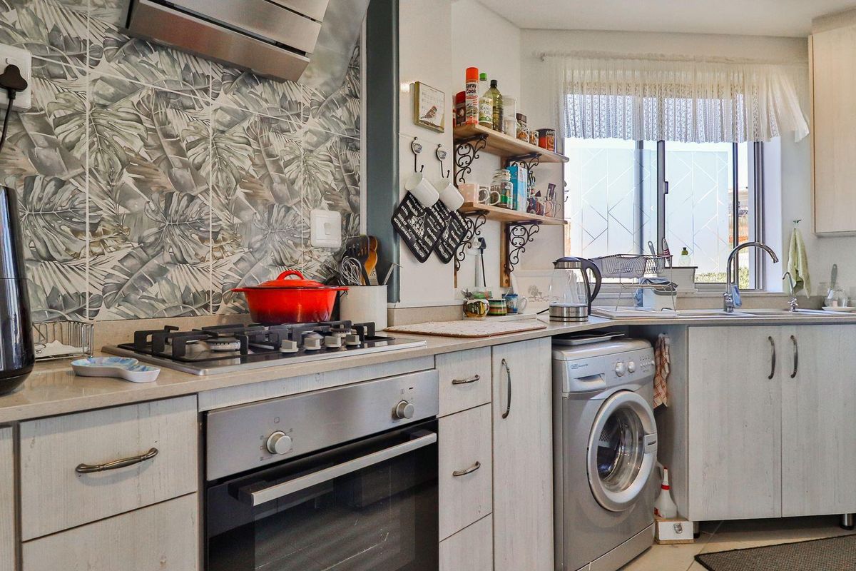 A functional kitchen featuring light-toned cabinetry, a gas hob with extractor fan, built-in oven, and an integrated laundry space with a washing machine.