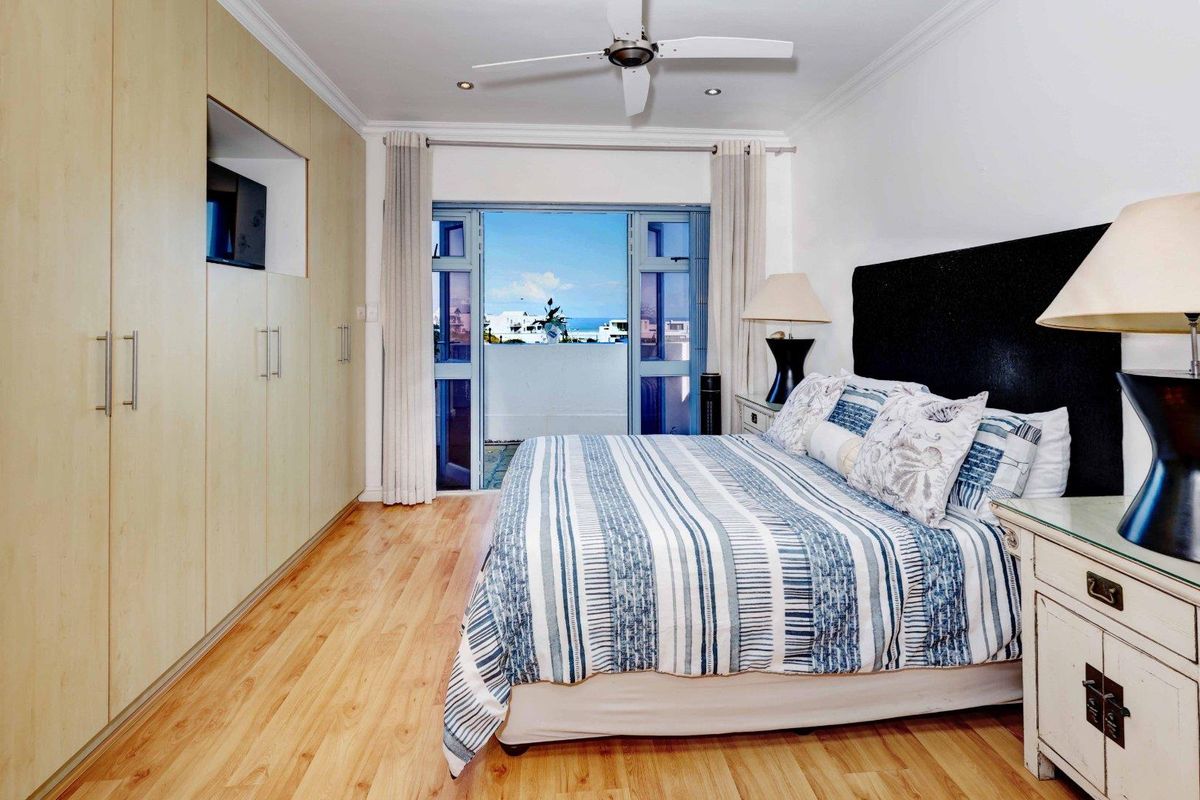 A well-maintained bedroom featuring light wood laminate flooring, extensive built-in cabinetry, a ceiling fan, and direct access to a private balcony with coastal views.