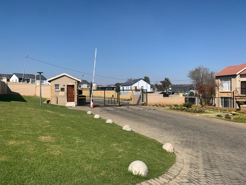 View of the secure gated entrance to the apartment complex, featuring a guard house, boom gate, and paved driveway access.