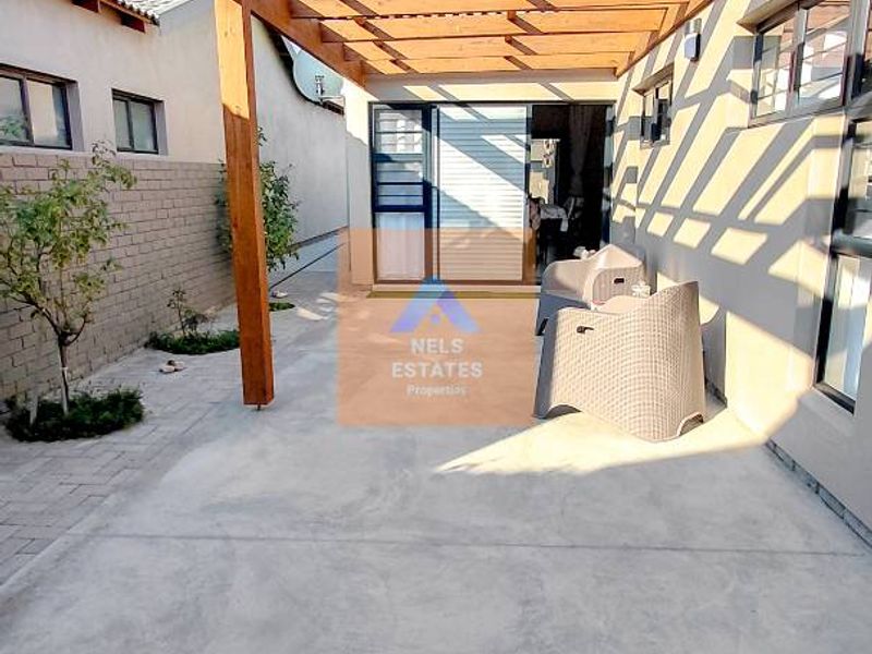 A well-maintained outdoor patio area featuring a timber pergola structure, concrete flooring, and direct access to the interior through sliding glass doors.