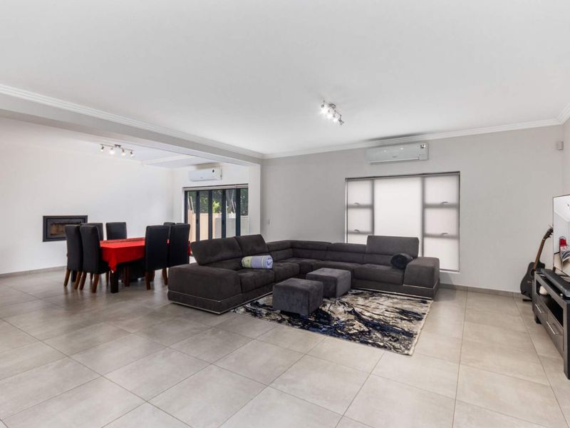 Spacious open-plan living and dining area featuring neutral tiled flooring, split-system air conditioning, a built-in fireplace, and large aluminium stacker doors leading outdoors.