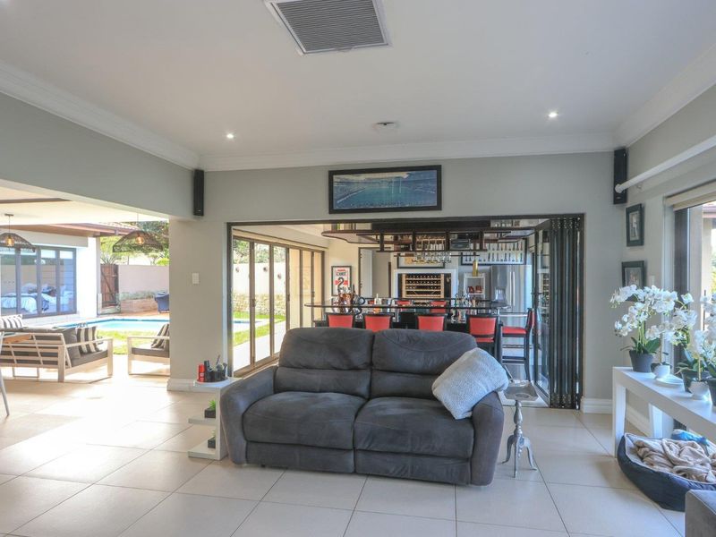 Spacious open-plan living area featuring tiled floors, ducted air conditioning, and seamless flow to an outdoor patio and built-in bar area.