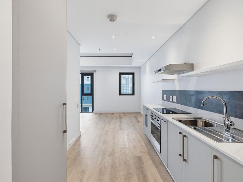 Modern open-plan kitchen and living area featuring sleek cabinetry, integrated appliances, laminate flooring, and recessed lighting in a clean, contemporary apartment setting.