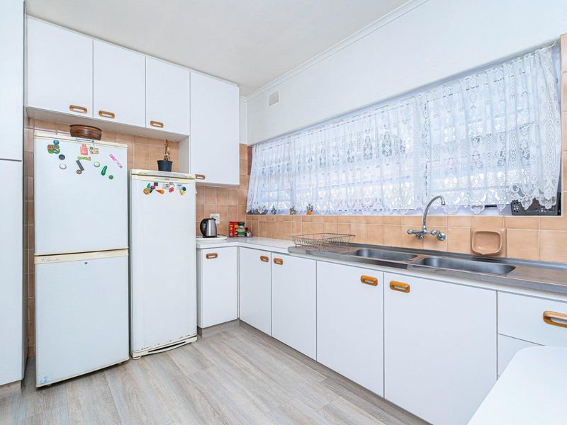 A functional kitchen featuring white built-in cabinetry, a double bowl stainless steel sink, and tiled splashbacks, offering a clean and practical workspace.