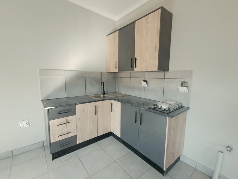A compact, modern kitchen featuring two-tone cabinetry, laminate countertops, a built-in gas hob, and a tiled backsplash.