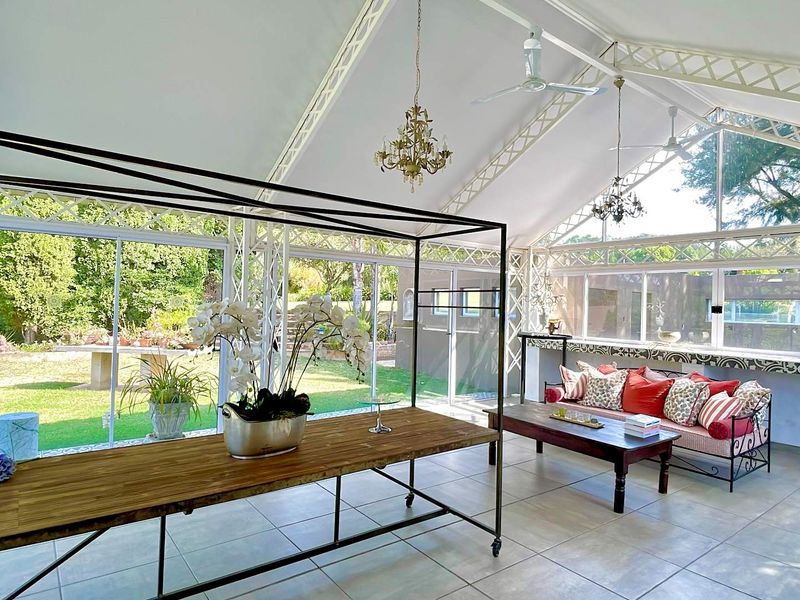 A bright and spacious enclosed patio featuring a vaulted steel truss ceiling, large glass sliding doors, and tiled flooring, offering views of the garden.