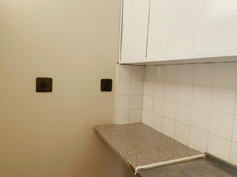 A compact kitchen area featuring white upper cabinetry, a tiled backsplash, and a laminate countertop with an integrated stainless steel sink.