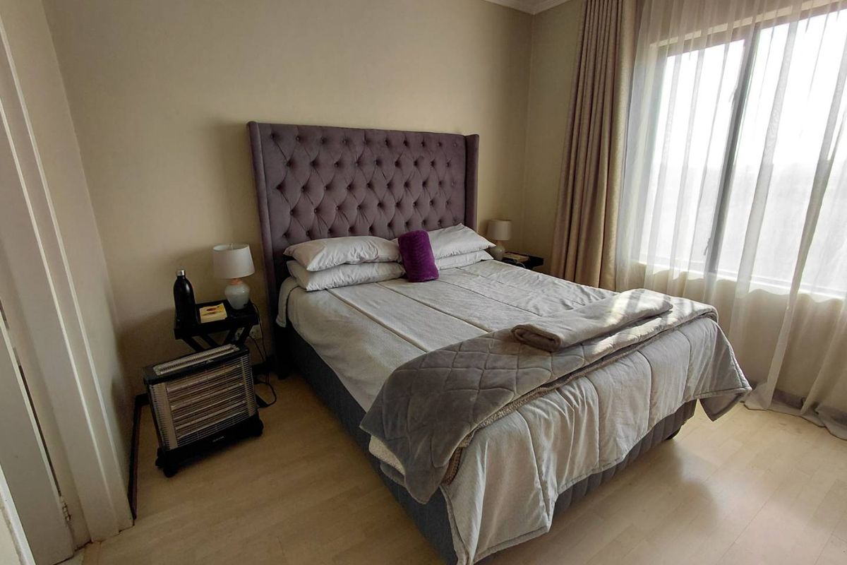 A well-maintained bedroom featuring light-toned laminate flooring, neutral wall finishes, and large windows with floor-to-ceiling curtains for natural light.